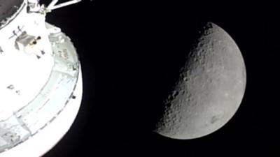 The moon is half covered in shadow, showing off its craters, with the capsule in the left of the photo