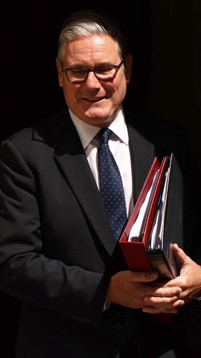 Starmer smiles as he holds a folder
