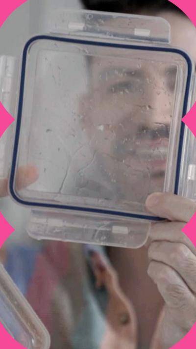 A man with brown hair and a moustache looks through the wet lid of a plastic food container. He is wearing a vertically striped shirt in blue, red, brown, green and coral.