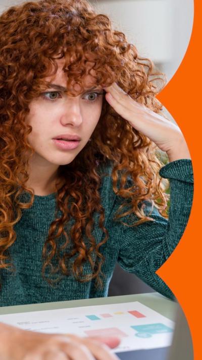 A woman with long curly red hair, looking shocked and annoyed, staring at a laptop.