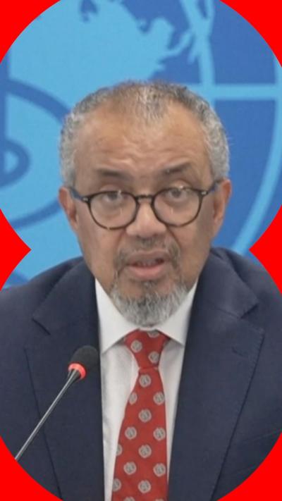 Tedros Ghebreyesus looks at the camera as he speaks at a press conference. He wears a navy blazer, white shirt and red tie.