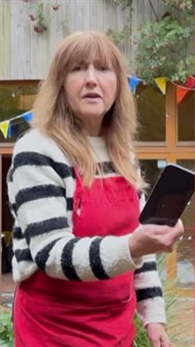 A woman outside with red apron holding a black phone.