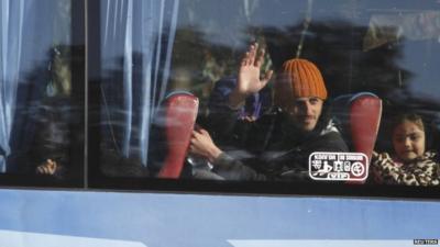 A man waves from the window of a bus