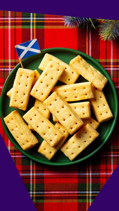 A plate full of Scottish shortbread with a little Scottish paper flag on one side. The plate rests over a plaid tablecloth.