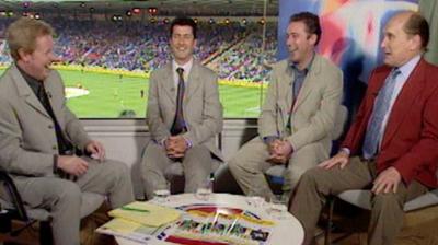 Four men sat in a football stadium TV studio round a low desk, all laughing.
