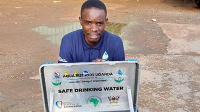 Timothy Kayondo squatting behind Eco Mobile Purifier