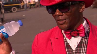 Farai sells water wearing a pink jacket with matching hat and bow tie