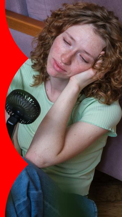 A woman with shoulder-length curly hair leans on a couch while holding a fan