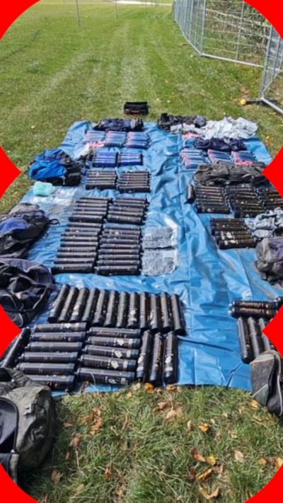 Dozens of packets of drugs laid out on a blue groundsheet in a field.