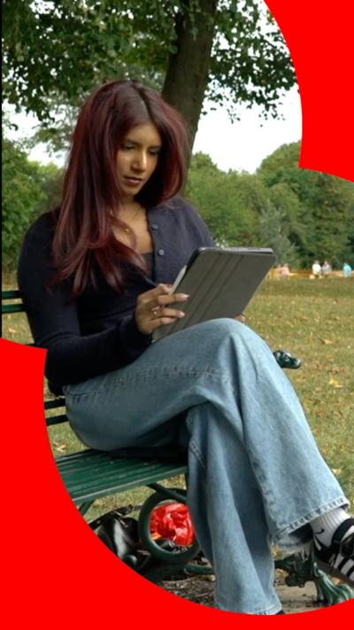 A female medical student sat on a park bench and looking into a tablet.