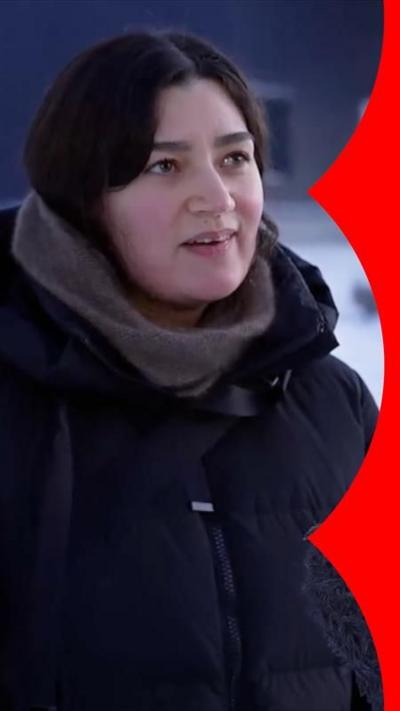 Woman with black hair, wearing a black jacket, being interviewed in the snow.