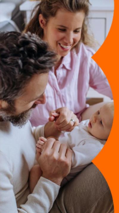 A dad sat on the floor with baby on his lap. Mum looks on from his side.