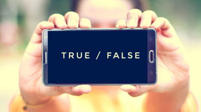 A pair of hands holding a mobile phone out in front of them. On the screen it reads "True / False"