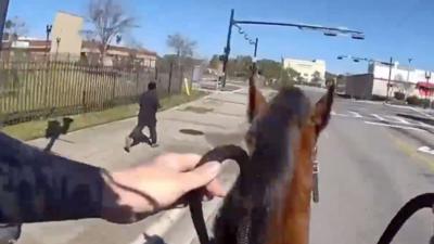 A man runs from a mounted police officer seen through the POV of the officers body camera.