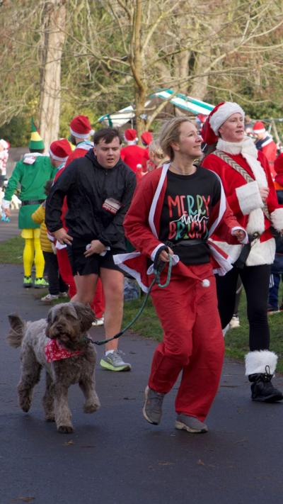 A woman in a Santa costume running with her dog