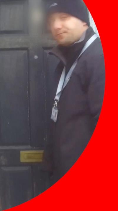 A person in a black jacket and beanie hat stands near a weathered black door.