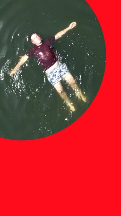 Man floating on his back in open water wearing a dark shirt