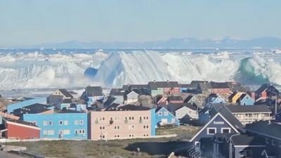 Iceberg collapsing creating wave near city with colourful houses