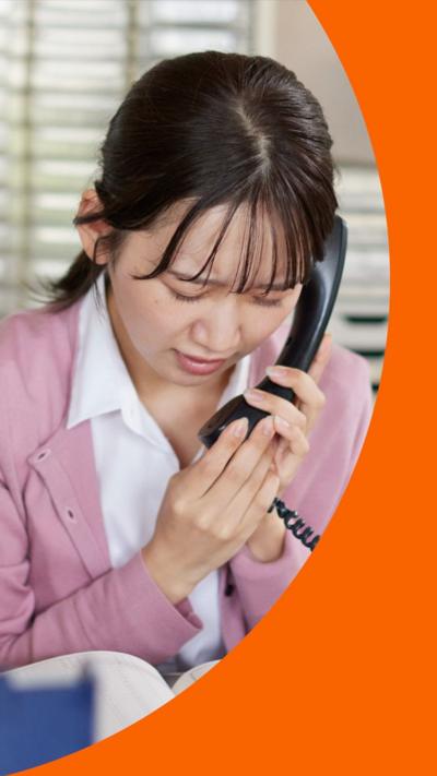 A woman looks stressed while on the telephone. She wears a white shirt and pink cardigan