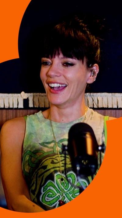 Lily Allen, wearing a green sleeveless top, in front of a microphone.
