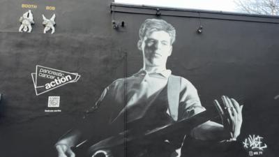 A black and white mural shows Andy Rourke from The Smiths playing his bass, with a Pancreatic Cancer Action logo and a QR code.