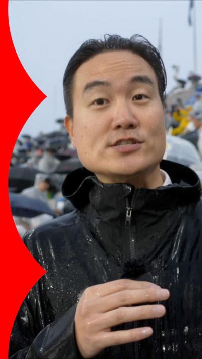 BBC correspondent Jake Kwon holding mic and wearing black rain jacket