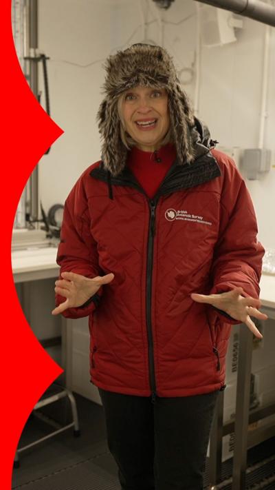 A woman in a large red coat wearing woolly trapper hat next to a pole of ice being shaved with a metallic tool