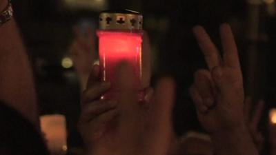 A candle is held aloft by the singing crowd at a vigil