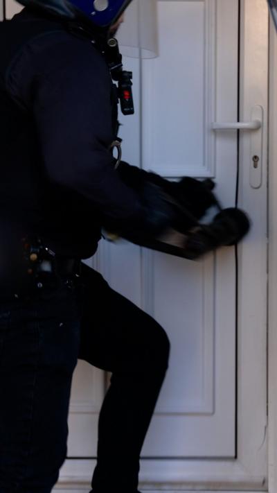 Police knocking down white door.