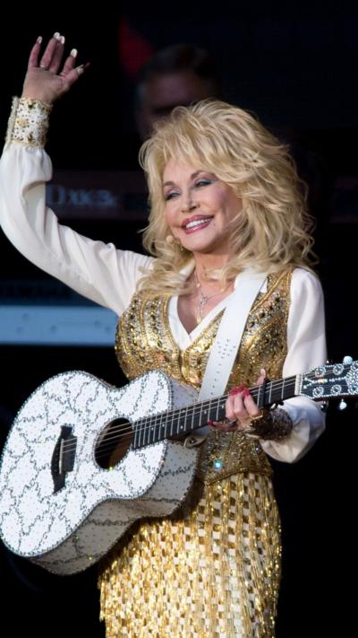 Singer Dolly Parton wearing white shirt, golden dress and holding white guitar