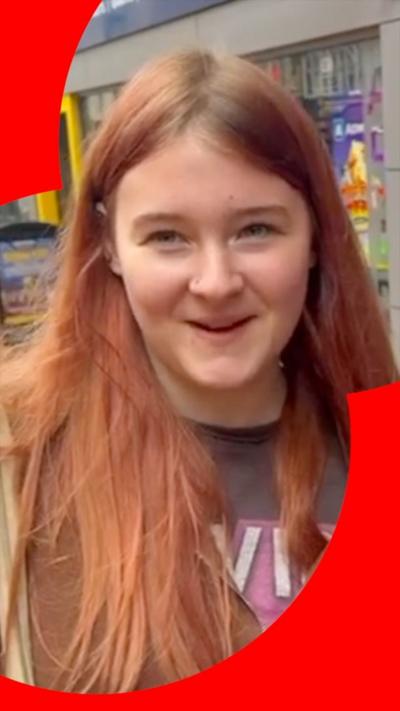 A woman with brown hair being interviewed on the street 