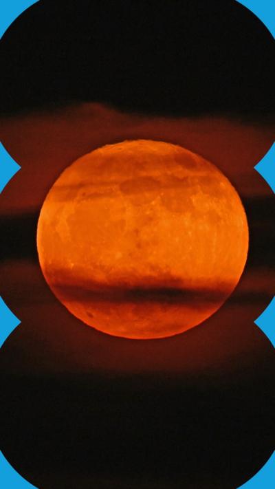 A strawberry moon in the night sky, seen through wisps of cloud.