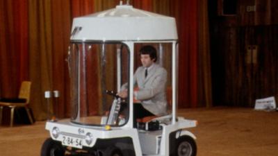 An unwieldy electric car driven around a hall