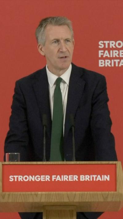 UK Defence Secretary Dan Jarvis speaking behind a podium, in front of red background