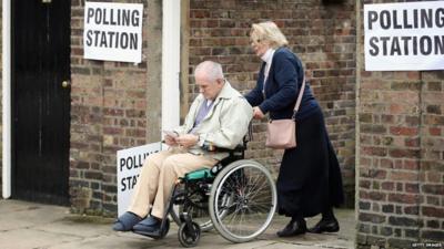 Polling station with a wheelchair user leaving the building, being pushed