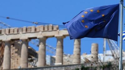 An EU flag flies in front of the ancient Parthenon temple