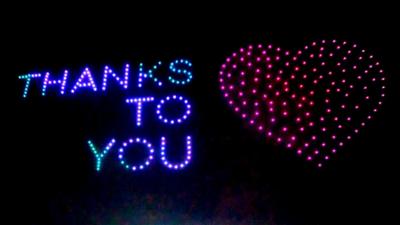 Lights in the sky spell out "thanks to you" with a heart symbol