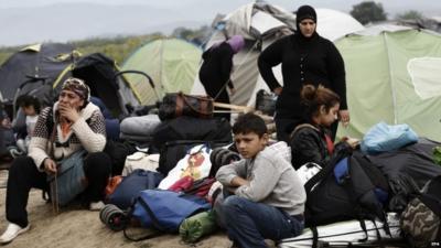 Members of a refugee family sit in front of their tent waiting to be transferred