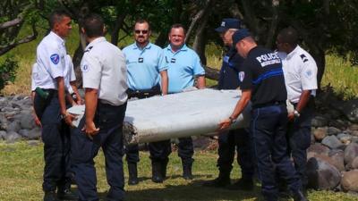 French gendarmes and police inspect a large piece of plane debris found on the beach in Saint-Andre, on the French Indian Ocean island of La Reunion