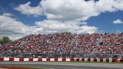 Spectators sit by the F1 track in Montreal. Blue skies and white clouds are overhead.