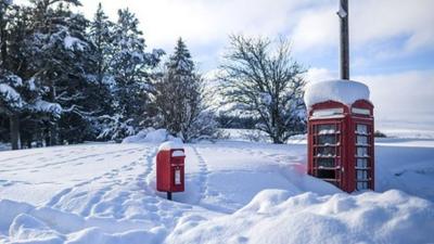 A red post box and phone box poke out of very deep snow