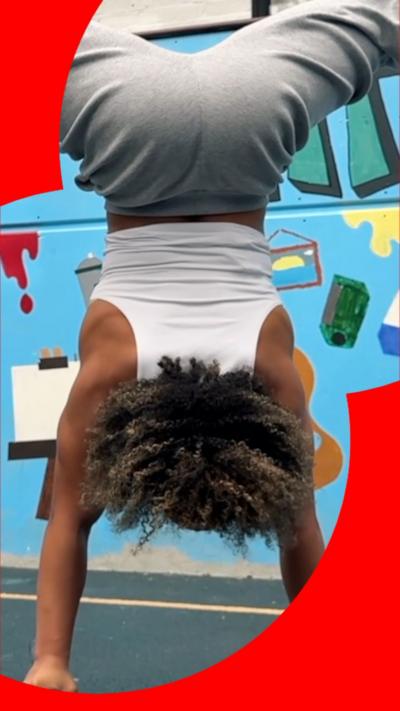 A woman wearing a white vest top and grey jogging bottoms does a handstand using two metal bars.