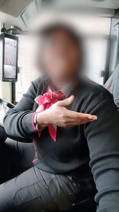A bus driver gestures with one hand while wearing a black sweater and a red bow tie.
