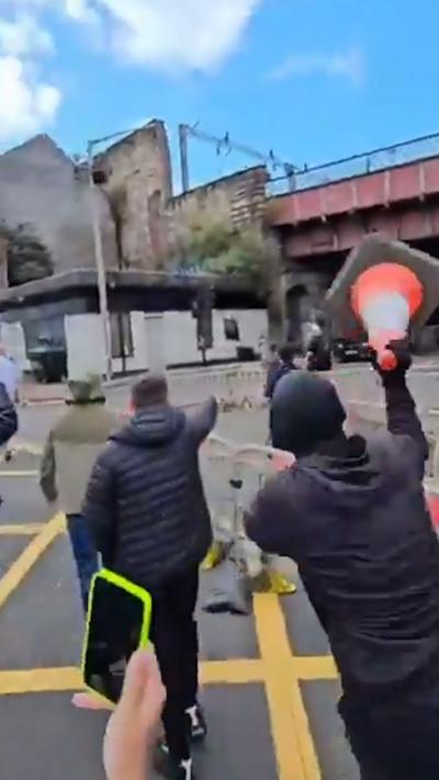 Group of protestors on Glasgow street, one poised to throw a traffic cone
