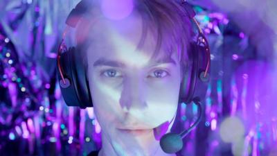 Young man with gaming headset on, lit by colourful lighting