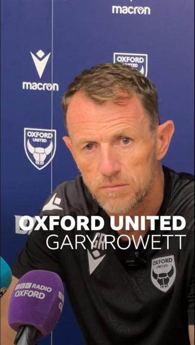 A middle aged man in a black sports top sat behind a purple Radio Oxford mic and in front of a purple Oxford United hoarding