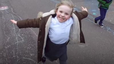 A young girl runs with her arms outstretched smiling at the camera