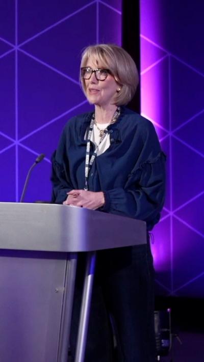 A woman with short hair and glasses is on stage