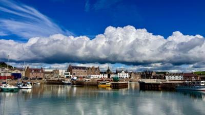 A huge shelf of thick white cloud across a harbour in Aberdeen with houses and the bay in front and blue sky above