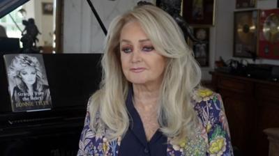 Bonnie Tyler sits in front of a piano with her autobiography on display